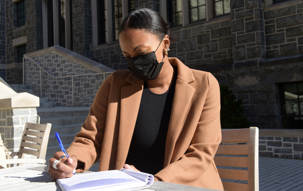 Catholic U student seated at outdoor table writing in notebook