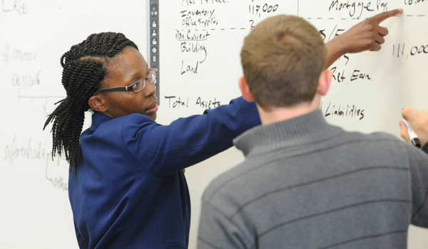 A professor and student working through a math problem on the white board.